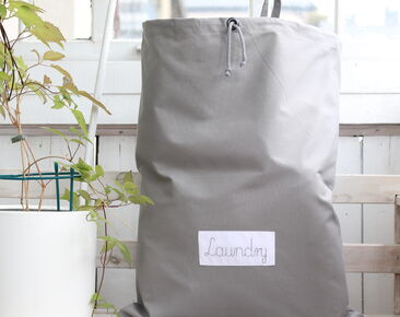 Didelis pilkas medvilninis skalbinių krepšys su pavadinimu